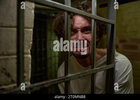 Portrait of crazy man with mad face crying bitterly in cage Stock Photo