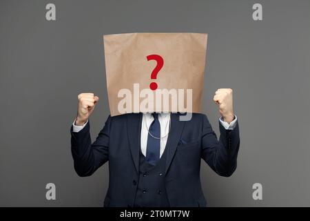 Corporate businessman hiding under paper bag with question mark on grey background Stock Photo