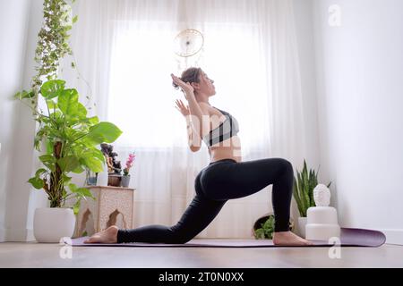 Young woman relaxing while doing yoga exercises on a mat at home. Sport concept. Stock Photo