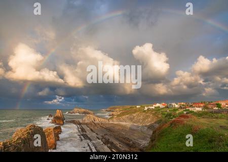 Full rainbow over sea coast with Arnia beach in Santander, Cantabria, North Spain with cliffs and flysch rocks. Popular travel destination Stock Photo