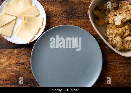 An empty plate on a wooden background stands next to a plate of cheese and deep-fried cauliflower Stock Photo