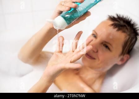 A woman takes a bath with foam. She pours gel onto her palm in the shower Stock Photo