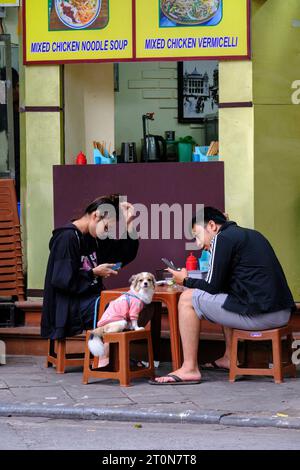 Hanoi, Vietnam. Couple Checking Cell Phones at a Sidewalk Coffee Shop. Stock Photo