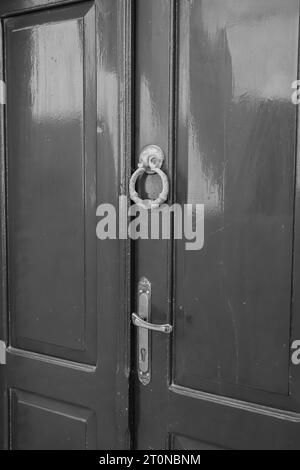 Black and white closeup of a wooden double door with metal hardware and antique cast iron door knocker in the Old Town of Rhodes, Greece Stock Photo