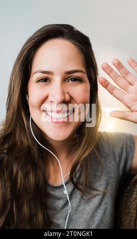 Hispanic woman smiling on video call with mobile phone at home - Pov girl streaming live on social app Stock Photo