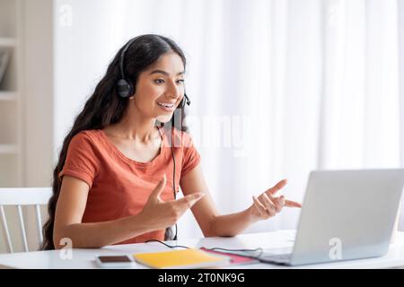 Cheerful remote worker pretty indian woman using laptop and headset Stock Photo