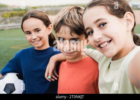 Kid friends after soccer play game having fun taking selfie in lawn - Latin children celebrating and hugging together - Childhood friendship and sport Stock Photo