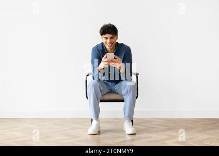 Middle eastern young man texting on smartphone over white wall Stock Photo
