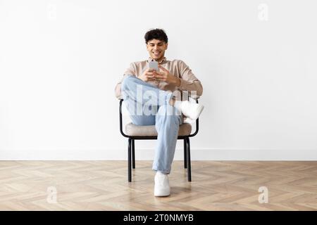 Arab Man Websurfing Via Cell Phone Sits In Chair Indoor Stock Photo