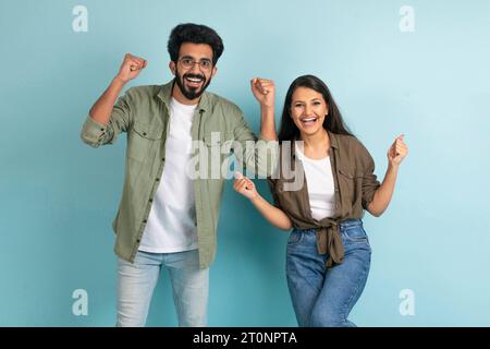Emotional millennial indian couple celebrating success on blue background Stock Photo