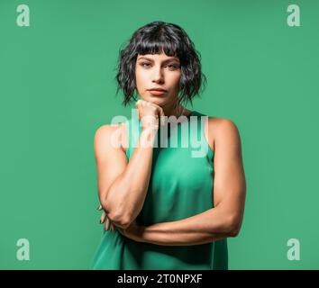A striking brunette model, dressed in a green tank top, poses with her chin resting on her fist, giving a deep and serious look towards the camera. Stock Photo