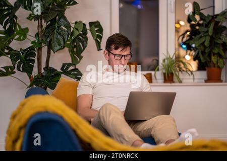 Man middle aged student working on educational project lying on couch at home in evening after job. Stock Photo