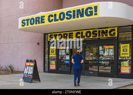Store entrance with store closing banners and signs advertising final days discounts with a shopper entering the store. Stock Photo