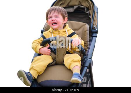 The unhappy child's face shows stress as he crying in the stroller during the park walk, isolated on white background. Kid aged two years (two-year-ol Stock Photo