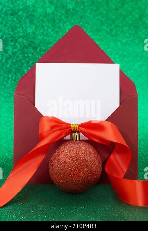 Christmas blank greeting card mockup with red glitter ball with bow and ribbon on sparkling green background. Envelope with letter with white paper. V Stock Photo