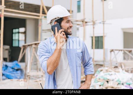 happy foreman builder using smart phone calling business contact in construction site. construction engineer or architect with modern connection techn Stock Photo