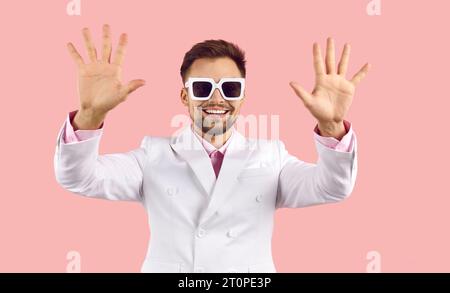 Happy handsome actor in white suit and sunglasses waving both his hands and smiling Stock Photo
