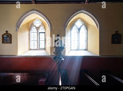 ST.HILARY CHURCH SUNLIGHT STREAMING THROUGH THE WINDOW ILLUMINATING STATUE OF JESUS Stock Photo