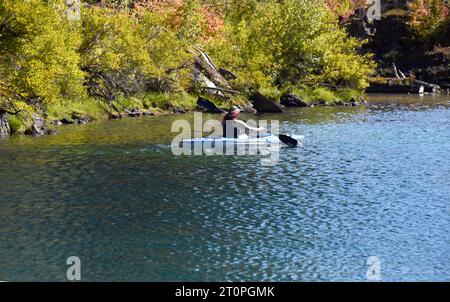 Woman paddles her kayak along the shore of Clear Lake in Oregon.  Her hair is dyed pink and she is wearing a tank top. Stock Photo