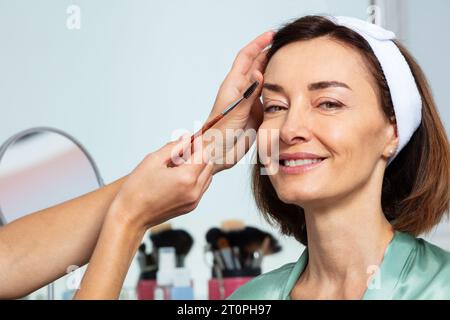 Beautician shape with eyebrow brush during makeup of a woman Stock Photo