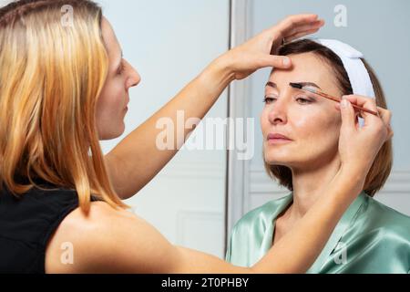 Beautician brushing using eyebrow brush on adult woman Stock Photo
