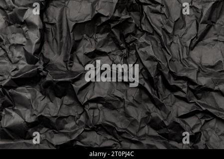 A sheet of black crumpled paper with folds and wrinkles. Dark paper texture Stock Photo