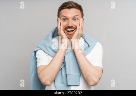 Happy man puts hands to cheeks in surprise, feels sincere happiness joy delight isolated background Stock Photo