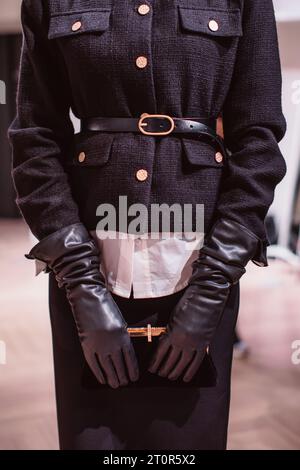 Fashion details of a classy black jacket, leather belt, gloves and classic velvet clutch. Fashion model posing on backstage Stock Photo