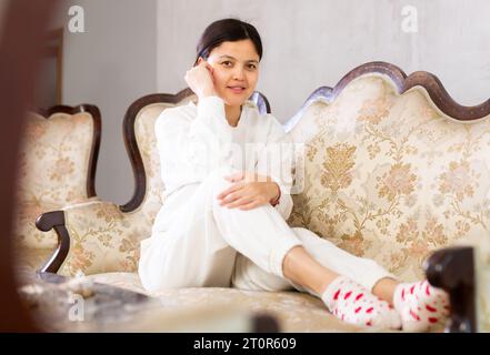 Relaxed young brunette sitting on soft antique sofa at home Stock Photo