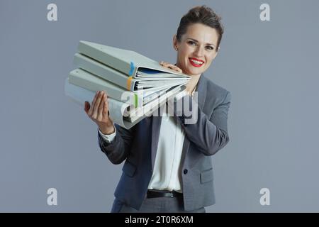 happy modern middle aged woman worker in grey suit with folders isolated on grey background. Stock Photo