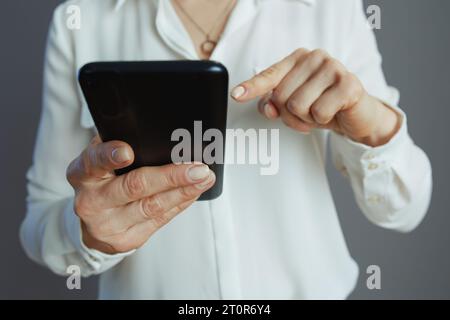 Closeup on small business owner woman in white blouse driving the growth of social media using smartphone isolated on gray background. Stock Photo