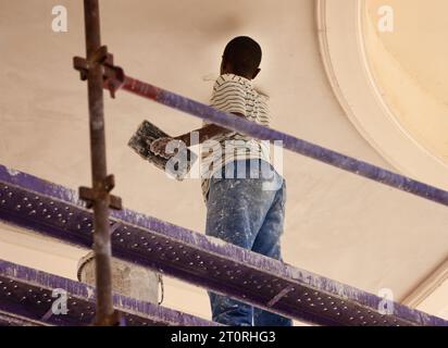 african construction worker climbed on scaffolding plastering a wall Stock Photo