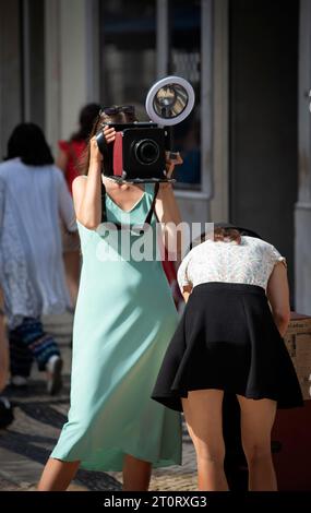 Rua Augusta, Lisbon Portugal.  A pair of young women setting up to take street portraits on a summer evening on Rua Augusta.  The wide pedestrian shopping street in central Lisbon’s Baixa Pombalina is paved with Portuguese traditional cobblestones. Stock Photo