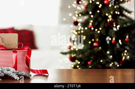 Christmas, New Year background with copy space for design. Empty wooden tabletop surface, blurred defocused decorated Christmas fir tree composition, bokeh sparkle lights effect, red boxes with gifts Stock Photo