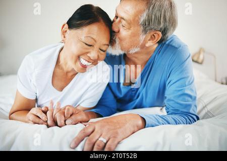 Love, holding hands and senior couple on bed for bonding, kissing and relaxing together at home. Happy, care and elderly Asian man and woman in Stock Photo