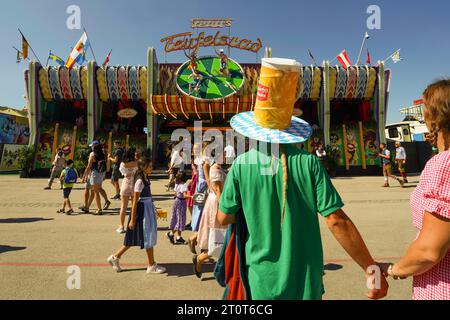 Munich, Germany, Europe - Sept.16, 2023. Oktoberfest beer festival grounds with rides, food, beer tents, beer gardens. Person in fun beer hat costume. Stock Photo