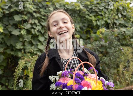portrait of a cheerful laughing girl 7-8 years old with a bouquet of flowers in her hands. Happy childhood, joyful emotional children, positive child. Stock Photo