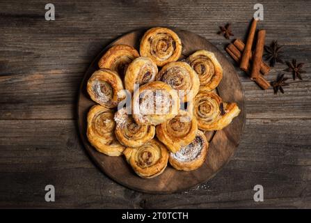 Freshly baked sweet and crispy cinnamon rolls. On a wooden plate, with powdered sugar Stock Photo
