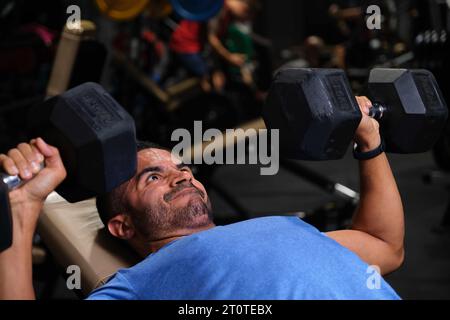 Strong Hispanic man doing dumbbell bench press at a gym. Stock Photo