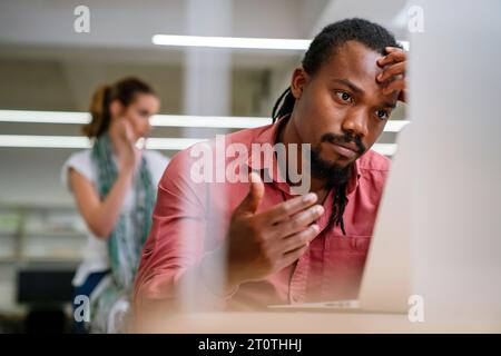 Stressful job. Stressed african businessman working at laptop, having problem at workplace. Stock Photo