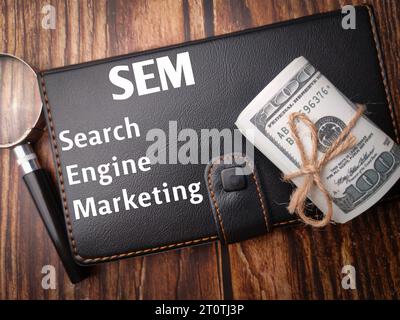 Top view banknotes,magnifying glass and notebook with the word Search Engine Marketing on wooden background. Stock Photo