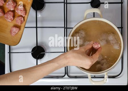 Top view of female hand dropping meatballs in boiling water Stock Photo