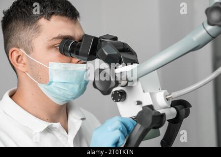 A doctor looks through a microscope in close-up. Dental microscope at work. The dentist is focused on solving the problem, setting up his equipment. Stock Photo
