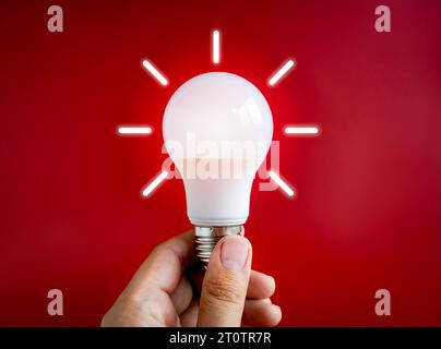 Glowing white light bulb with graphic radius neon style, holding by hand isolated on dark red background. Close-up creative lightbulb in creator's han Stock Photo