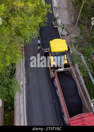 Aerial view of the construction of a new road as asphalt pavers, rollers, machinery, and workers come together to build a vital transportation link. W Stock Photo
