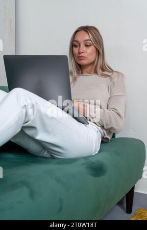Caucasian woman sitting on sofa and working on remote project on laptop in stylish living room at home Stock Photo