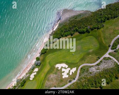 Aerial view of the golf course stretches out beneath, its lush green fairways complementing the breathtaking coastal panorama. Among the picturesque l Stock Photo