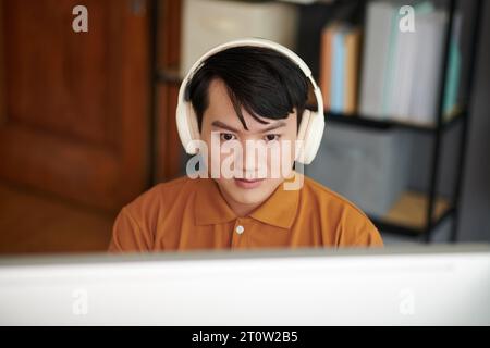 Young Asian software developer wearing headphones when working on computer in home office Stock Photo