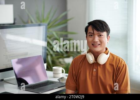 Portrait of smiling Vietnamese programmer sitting at desk in his home office Stock Photo
