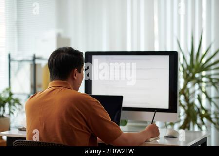 Software developer reviewing programming code and taking notes in planner Stock Photo